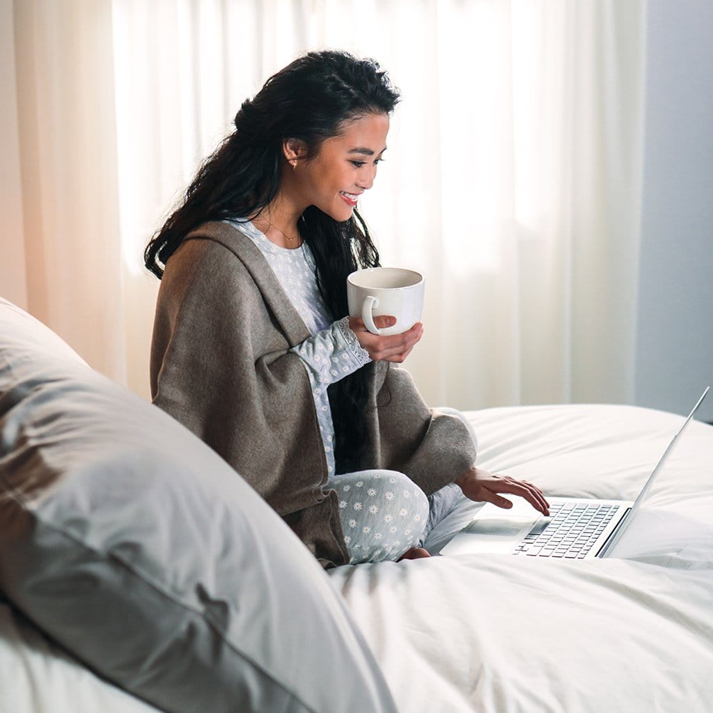 Woman holding coffee in bed featuring refined sateen sheet set