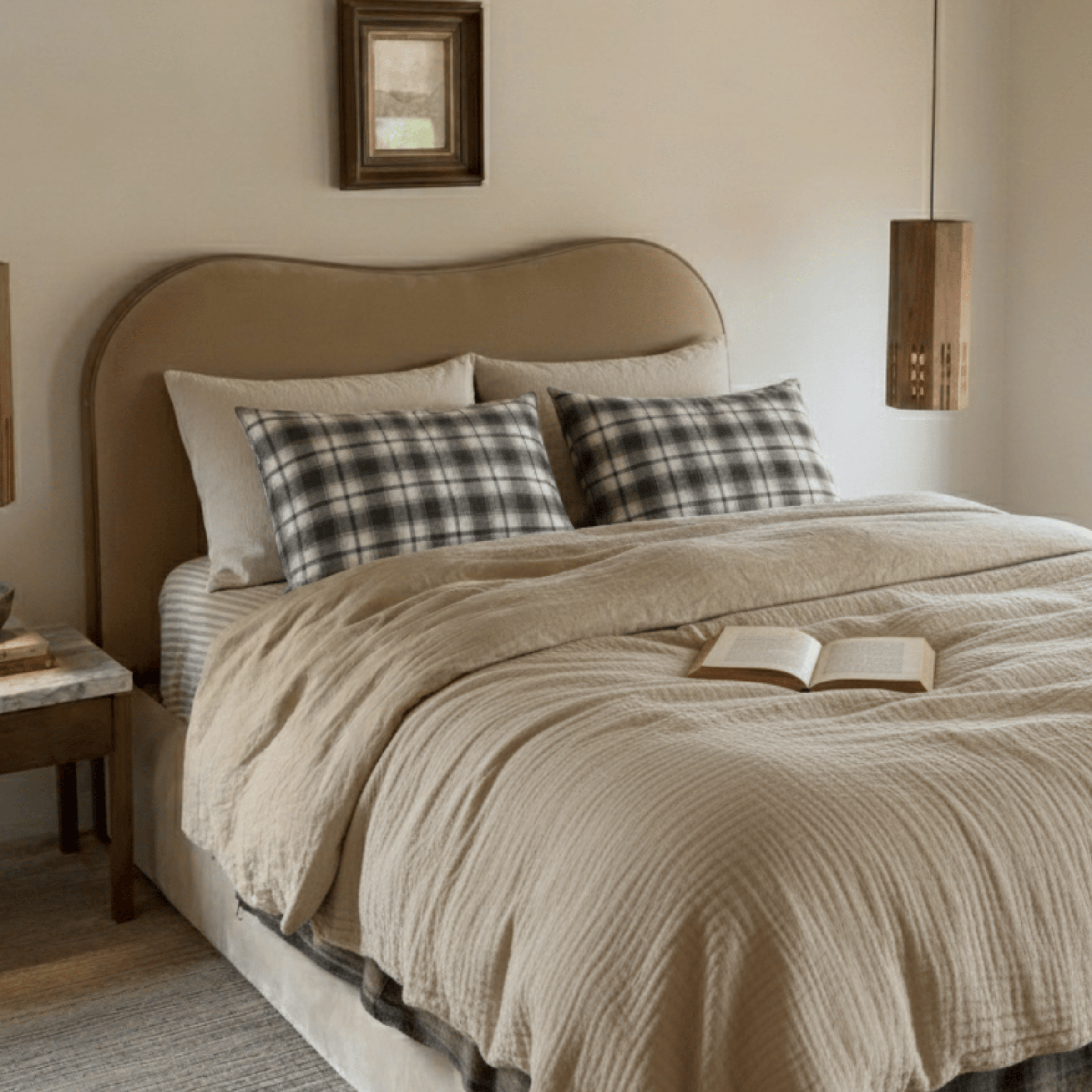 Neatly made bed with beige bedding and plaid pillows in a bedroom setting.