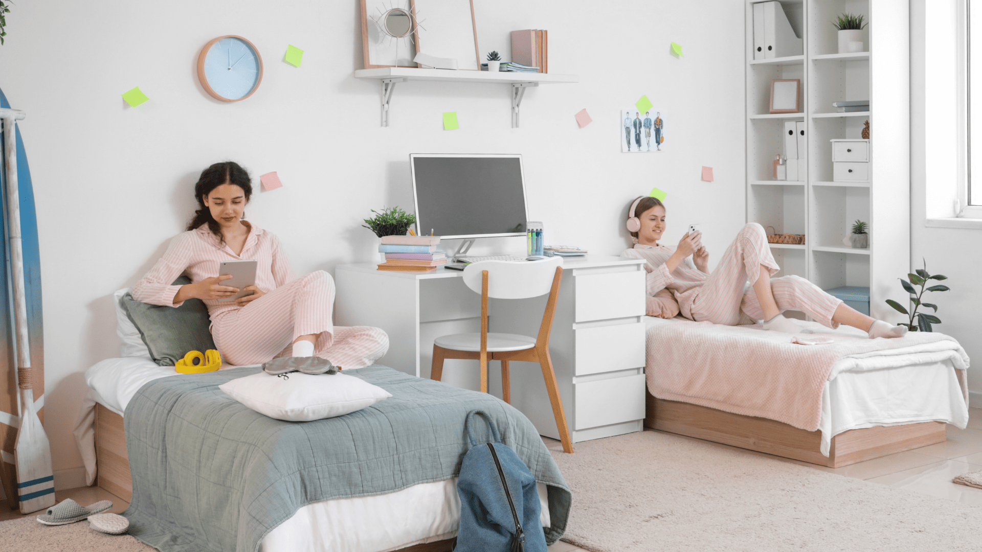 Two women in a shared bedroom with a desk, shelves, and bedding.